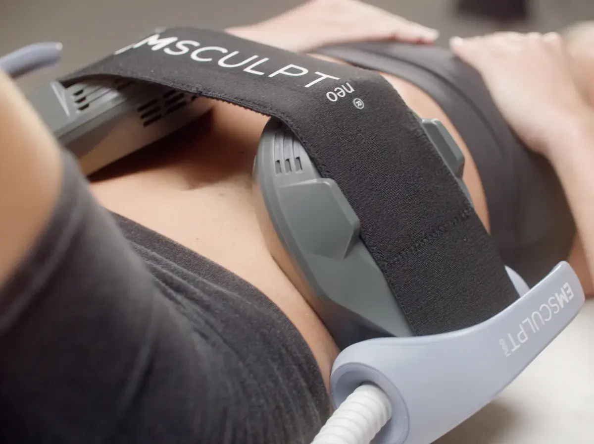Emsculpt Neo applicator on a woman's abdomen during a session